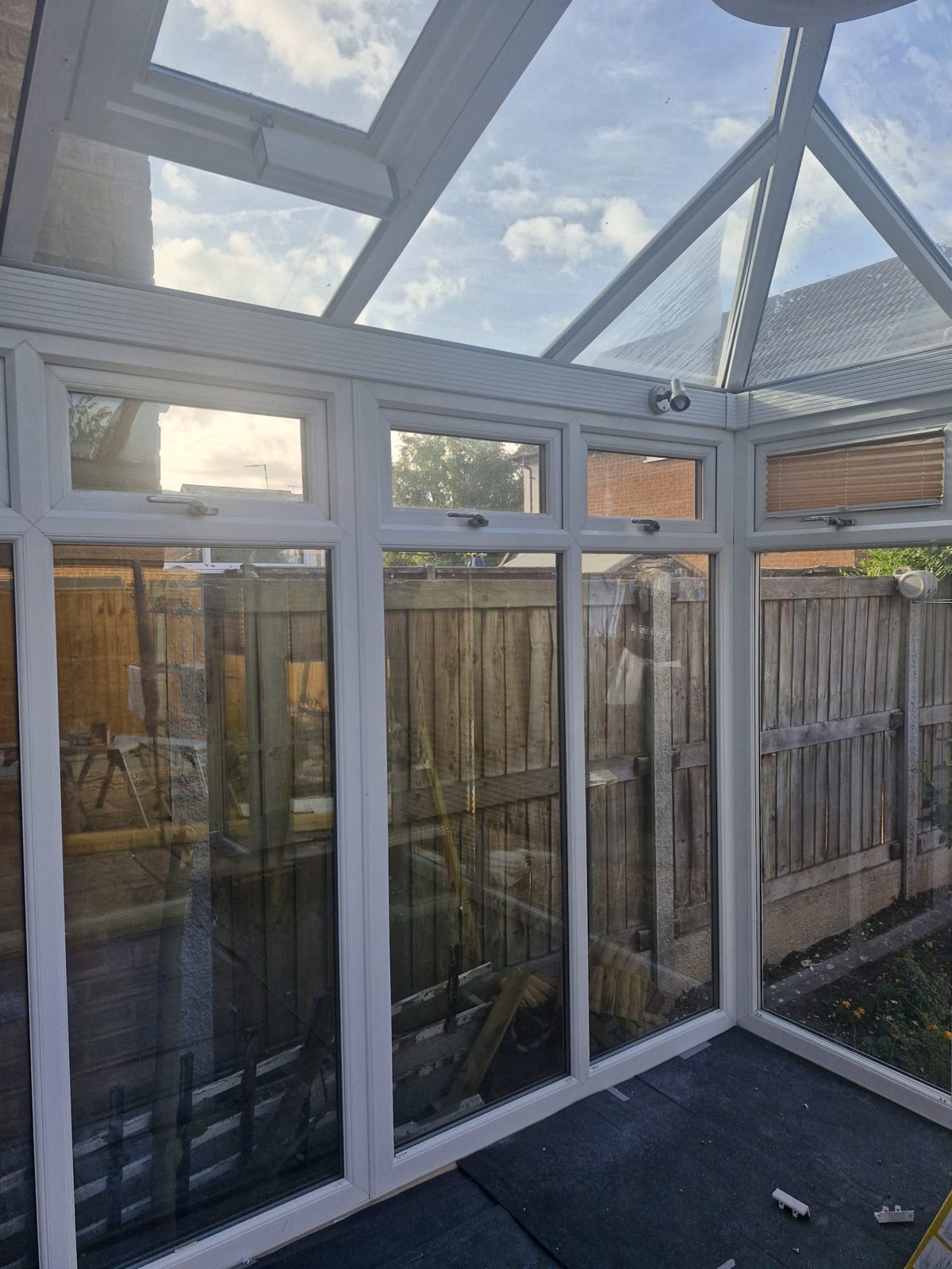 Luton conservatory before work, with full-height glazed panels facing the boundary fence